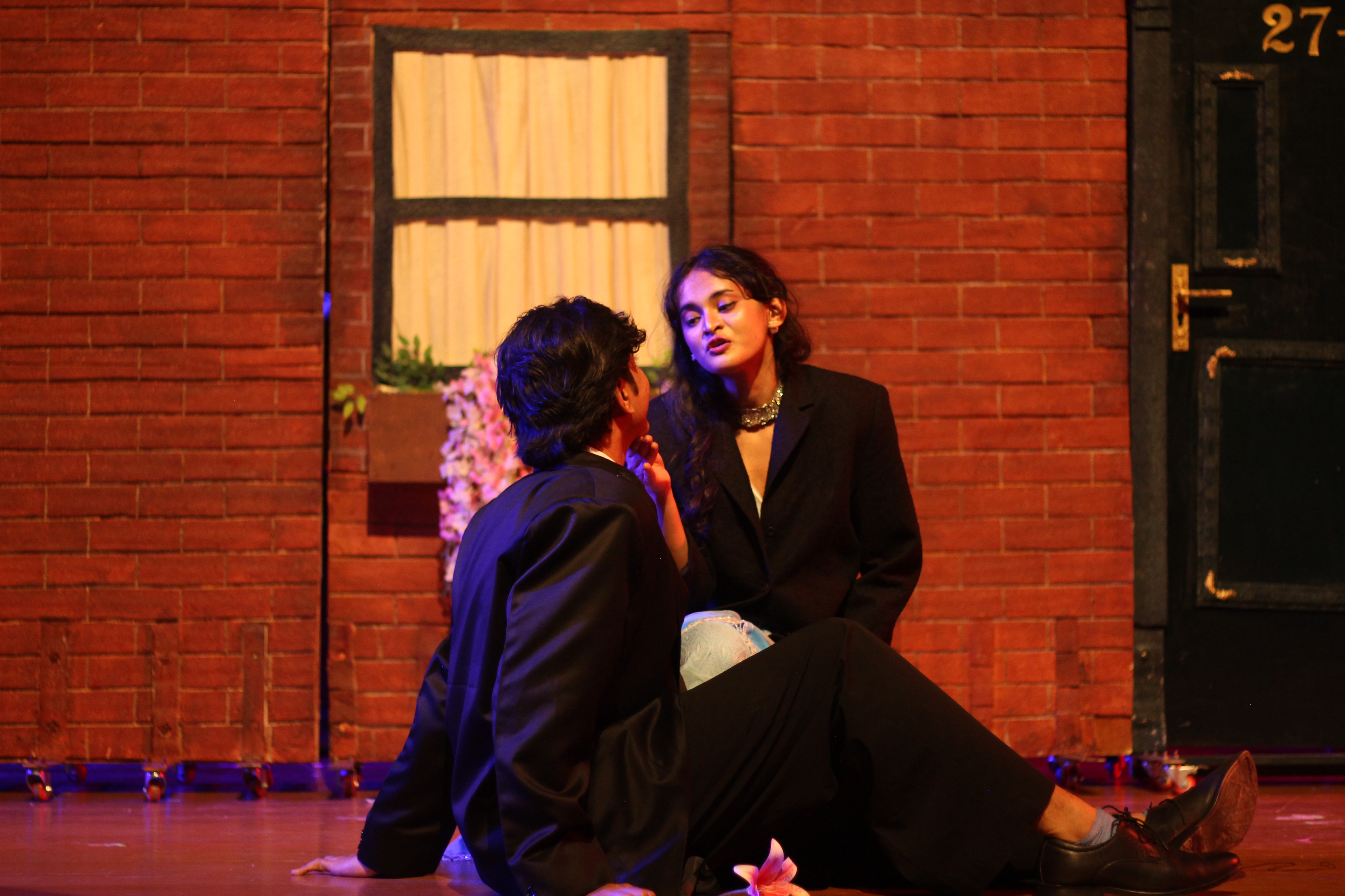 My Fair Lady actors performing an intimate scene against a brick house set under warm stage lighting.